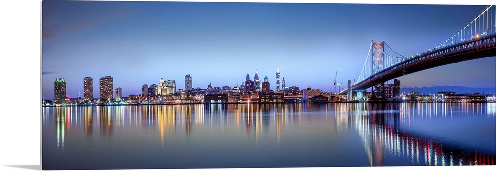 Panoramic photo of the Philadelphia city skyline reflected in the water at night, with the Benjamin Franklin Bridge on the...