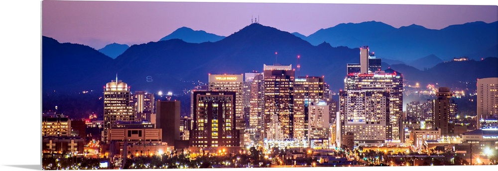 Panoramic photograph of a colorful sunset over the Phoenix, Arizona skyline with silhouetted mountains in the background.