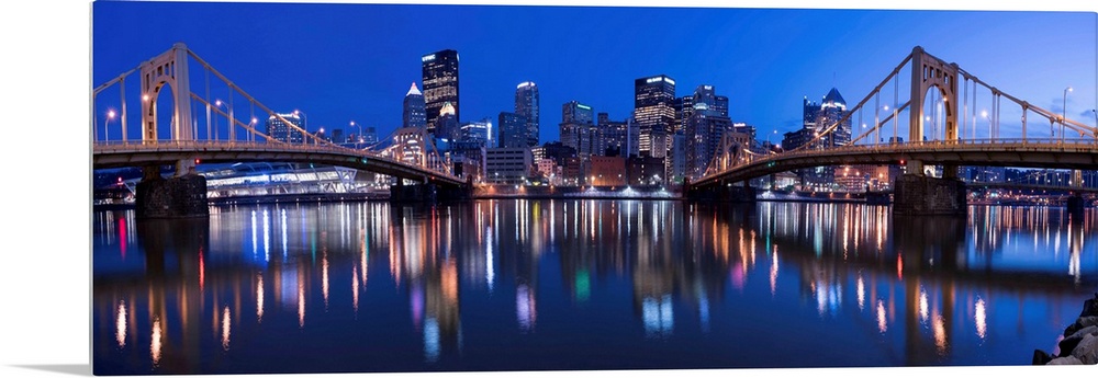 Panoramic view of the Pittsburgh city skyline in the evening reflected in the water, with two of the Three Sisters bridges...