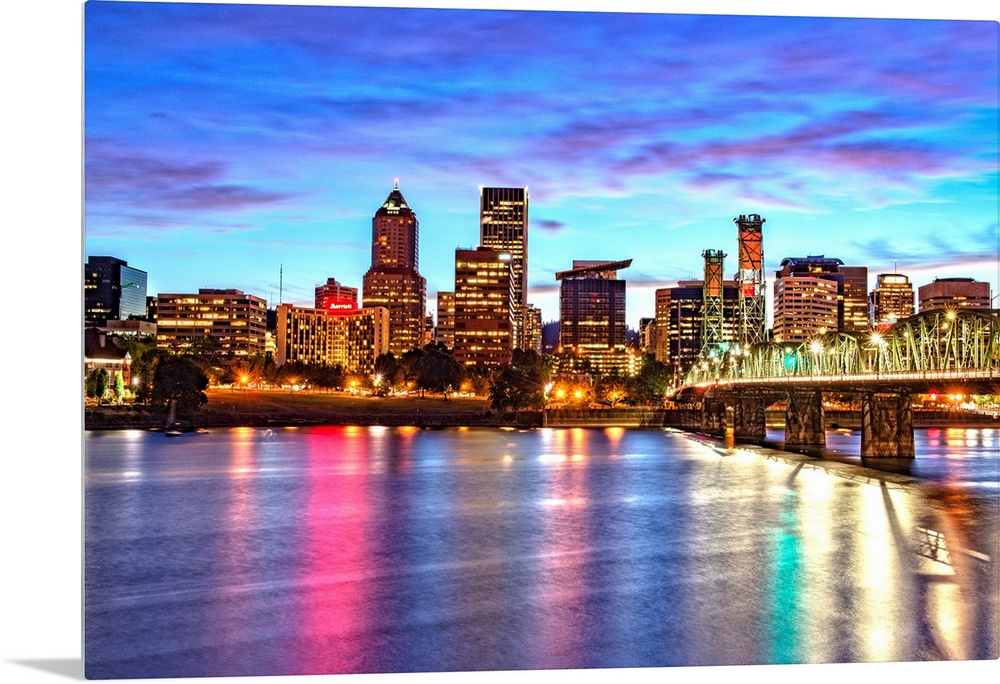 Photograph of the Portland, Oregon skyline lit up at sunset with colors reflecting onto the Willamette River in the foregr...