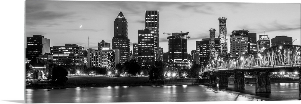 Panoramic photograph of the Portland, Oregon skyline lit up with lights at the beginning of sunset with a small crescent m...