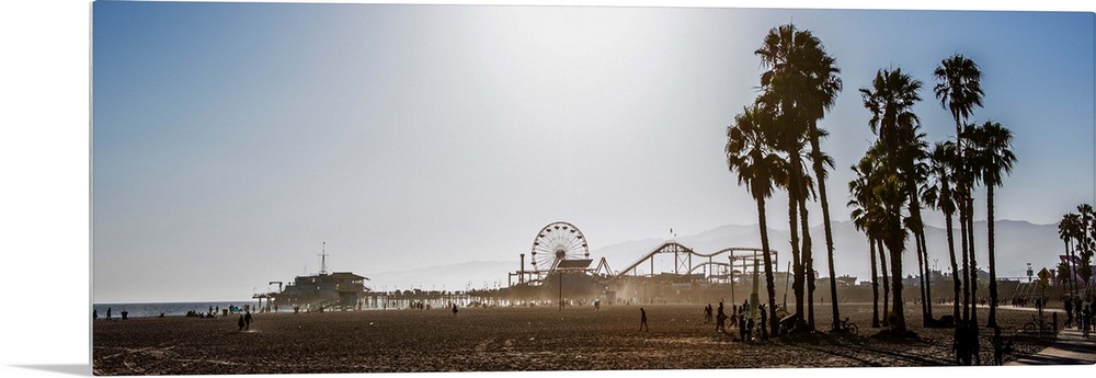 Panoramic photograph of the Santa Monica Pier in Los Angeles, California, with palm trees in the foreground and a purple h...
