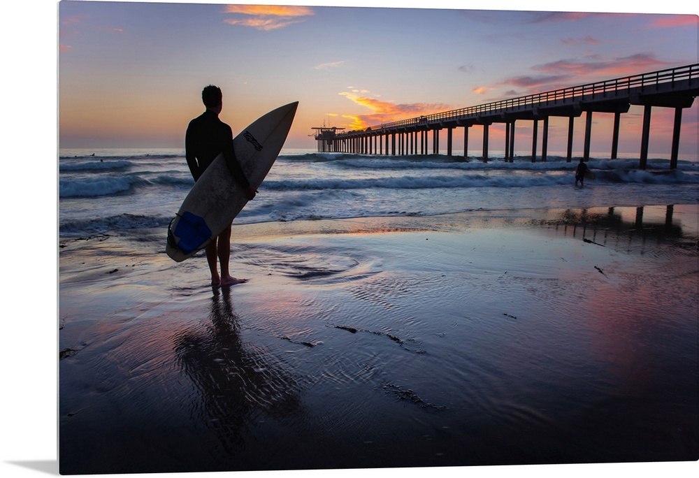 Silhouetted photograph of a man holding a surf board on the shore of Ocean Beach in San Diego, California, with the Ocean ...