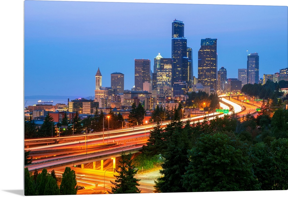 Photograph of the Seattle skyline at dusk with light trails from the cars on the highway in the foreground.