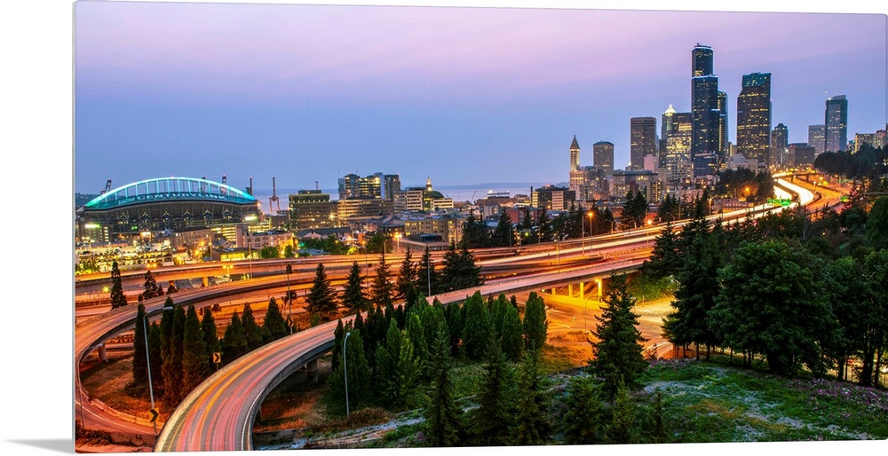 Panoramic photograph of the Seattle skyline at night with light trails from the car lights on the highway.