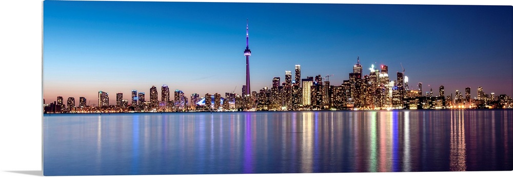 Panoramic photo of the Toronto city skyline with lights reflected in the water at night.