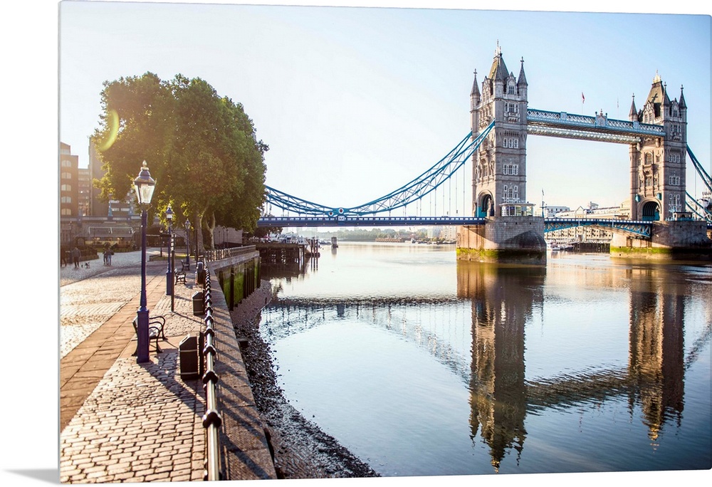 Photograph of Tower Bridge  reflecting on River Thames with a brick sidewalk on the side.