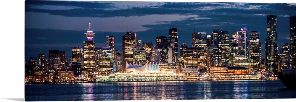 Panoramic photograph of the Vancouver, British Columbia skyline lit up on a dark blue night and reflecting bands of colorf...