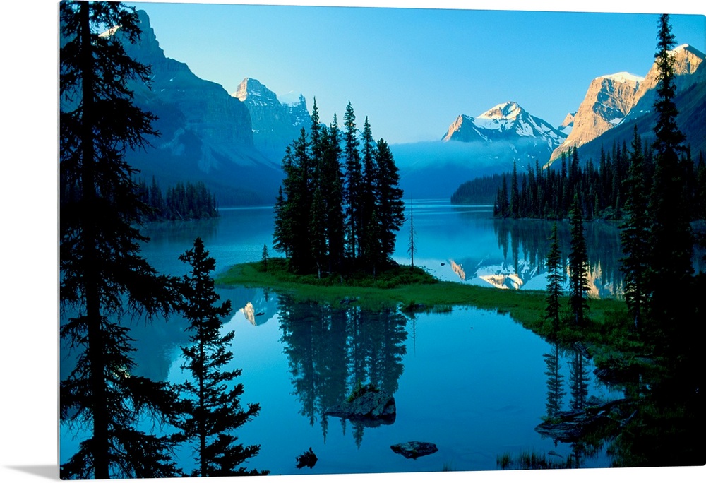 The northern landscape of evergreen trees and mountains reflect on the still waters of a lake in the morning.