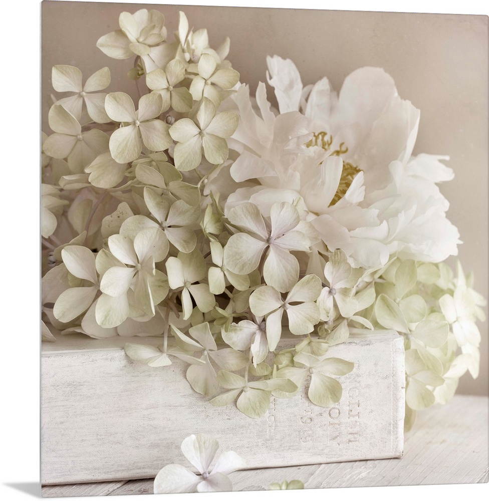 Square photo on canvas of white flowers laying on top of a white book with the spine facing the camera.