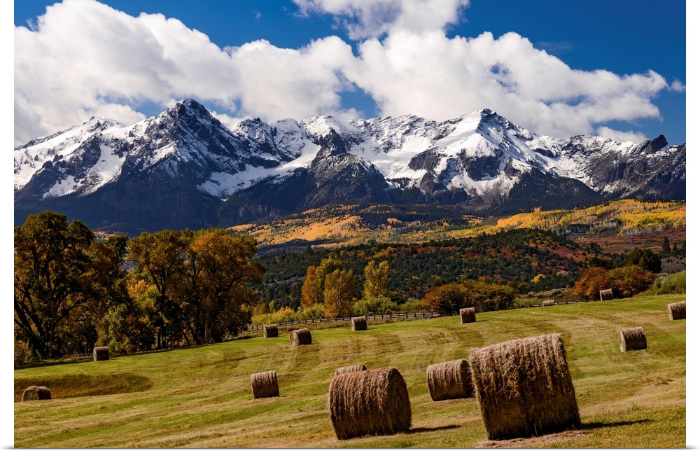 Grazing land at the foot of snow covered mountains and rustic autumn trees in a landscape photograph.