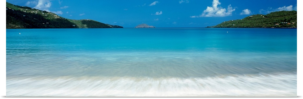 Panoramic photograph of clear water in a calm sea washing up a tropical beach.