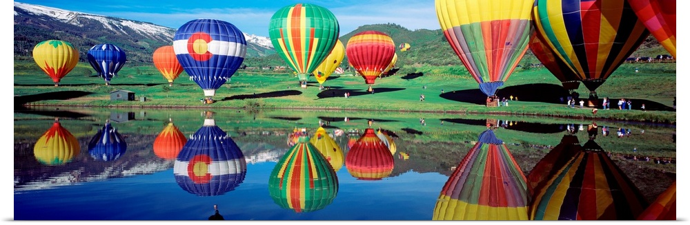 Vividly colored vehicles for the aeronautical sport gather around a lake and reflecting in the water.