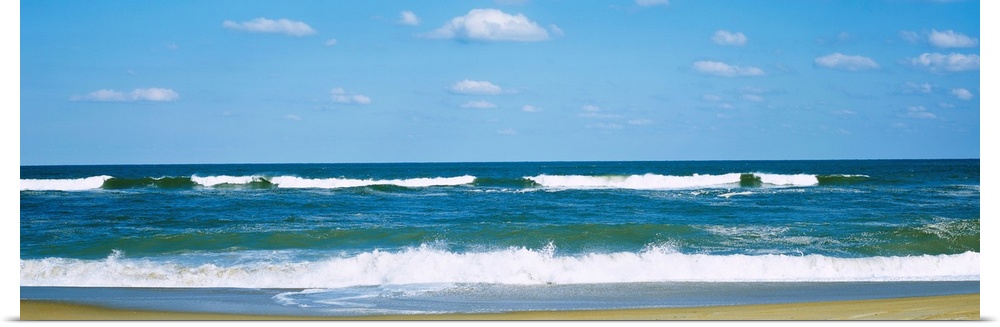 Panoramic landscape photograph of a clear day at the beach with waves washing up on the sandy beach.