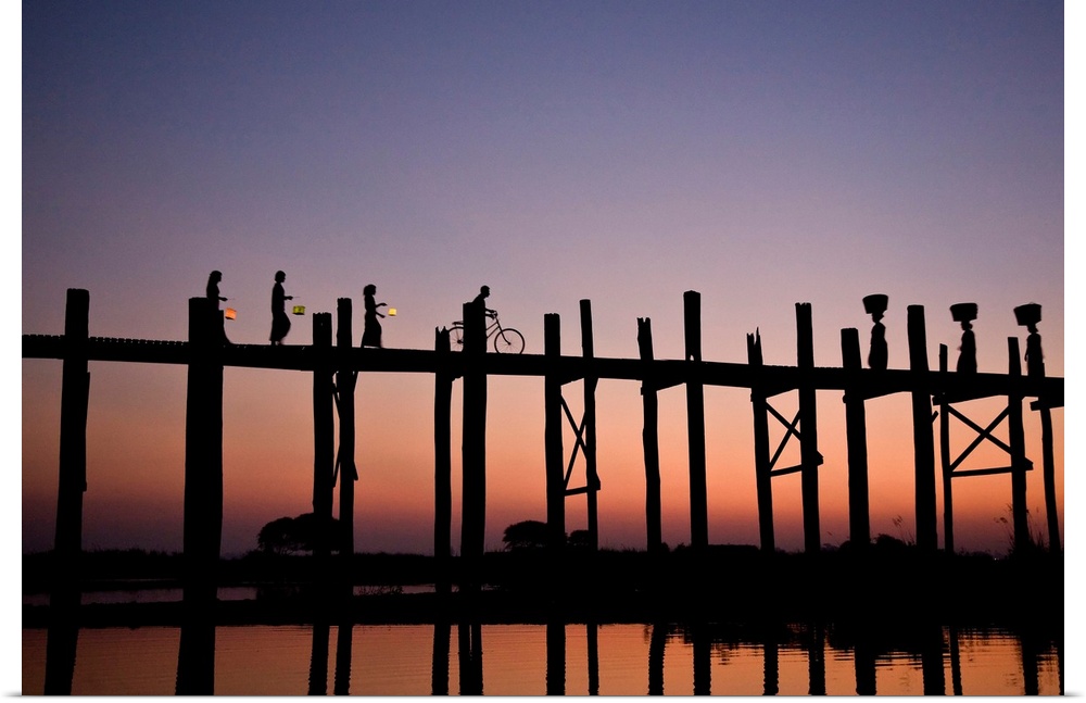 Photograph of people walking and biking across a bridge made of tall wooden beams over the ocean at dusk.  The bridge is r...