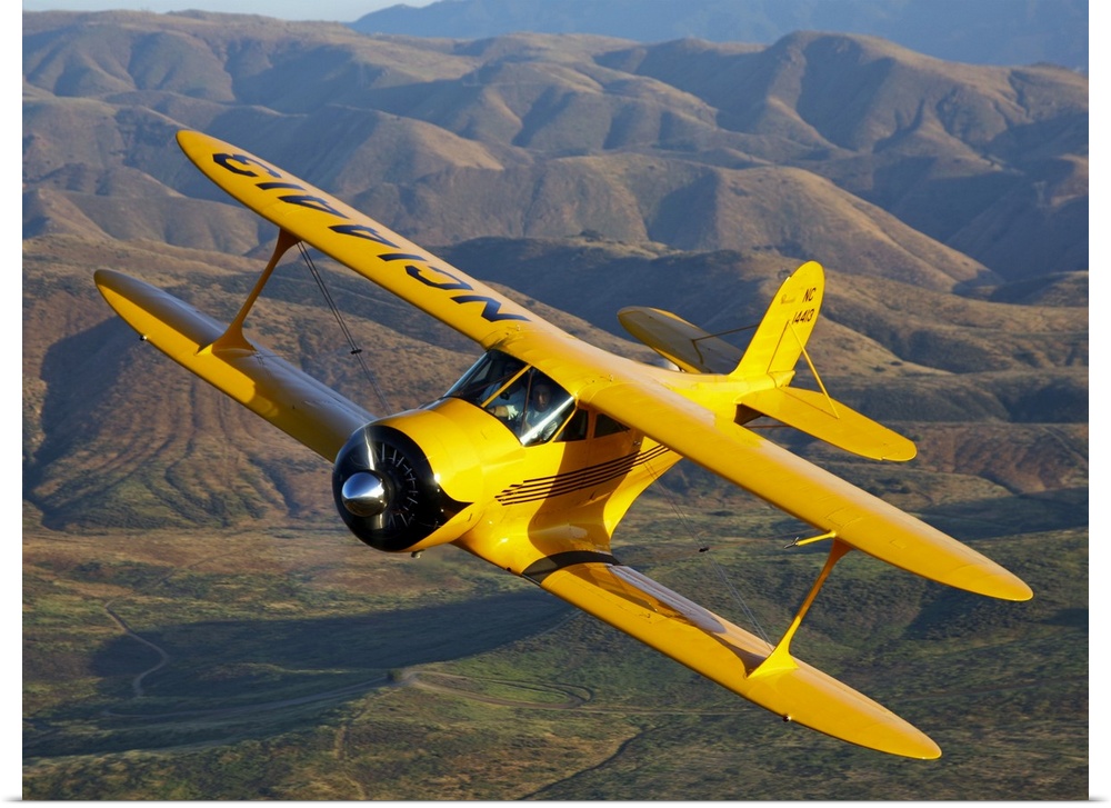 Photograph of a Beechcraft D-17 Staggerwing single propeller biplane flying over rolling hills.