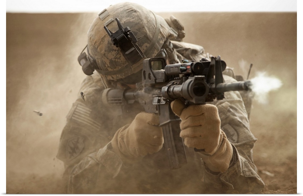 United States solider laying down in the desert sand and shooting a military rifle.