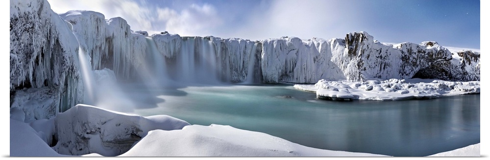 Icy snow covered landscape with waterfalls streaming down from cliffs surrounding a river.