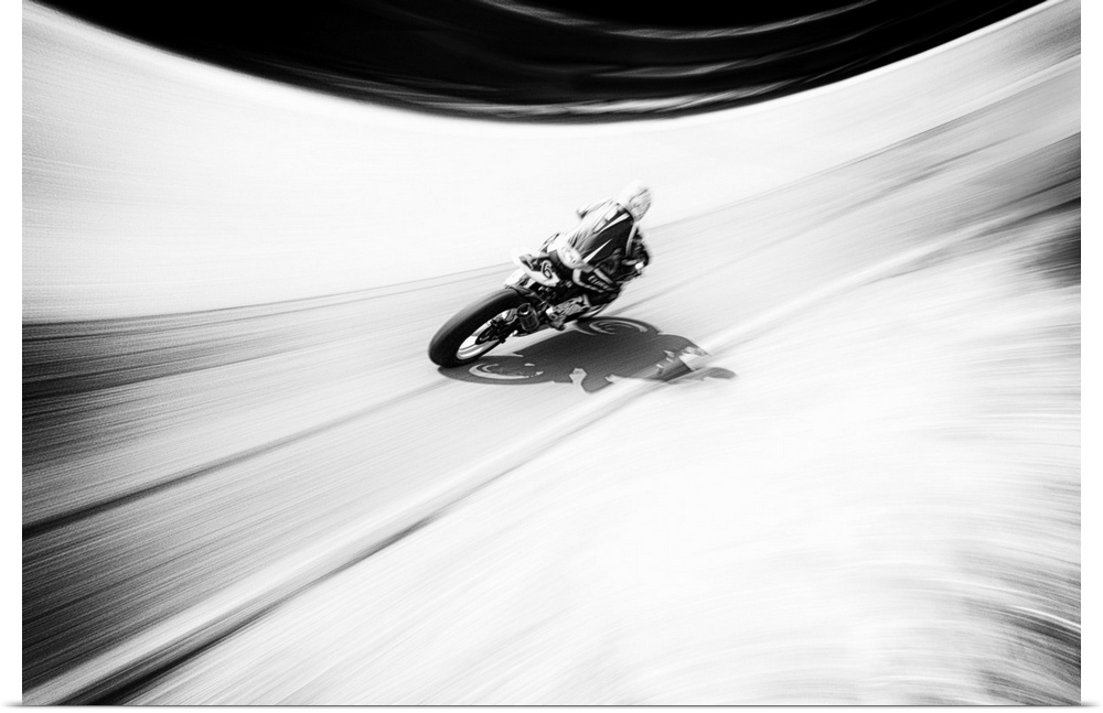 A figure on a motorcycle traveling fast on a curved road.