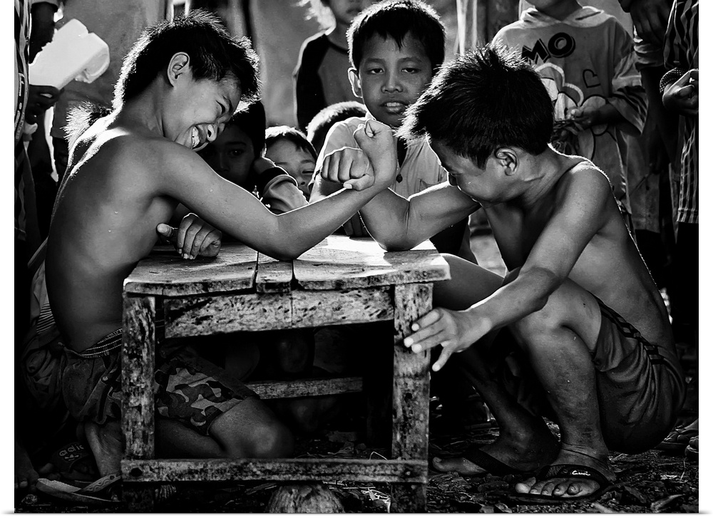 Children kneeling at a small table arm wrestling.