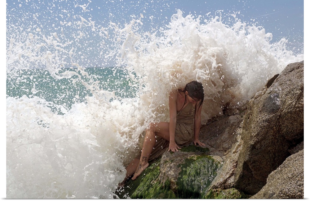 A model on ocean rocks braces herself against the crashing waves.