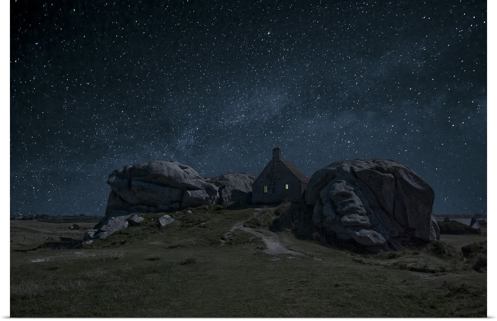 A small house nestled between large rock formations under a night sky full of stars.
