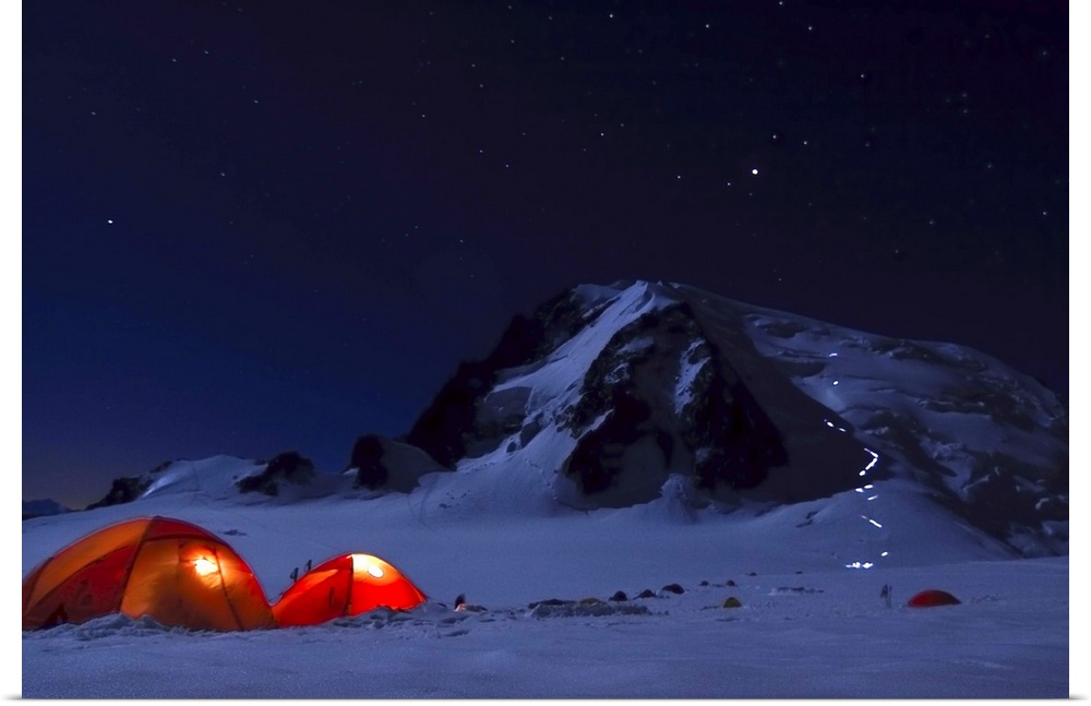 Camping tents set up at night at the bast of a snowy mountain in the alps.