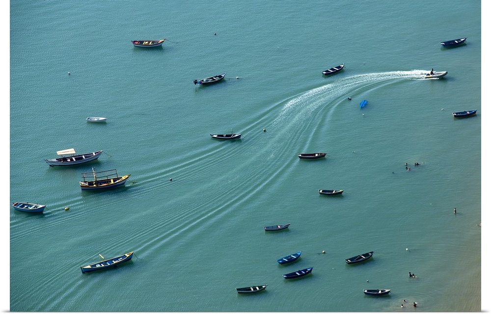 Aerial photograph of boats anchored on a teal ocean with wave lines creating movement from one motorboat in action.