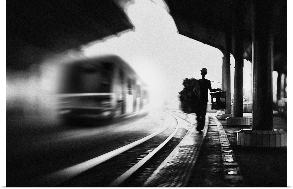 A man with luggage walks along a train station platform with a train on the rails nearby, Jakarta.