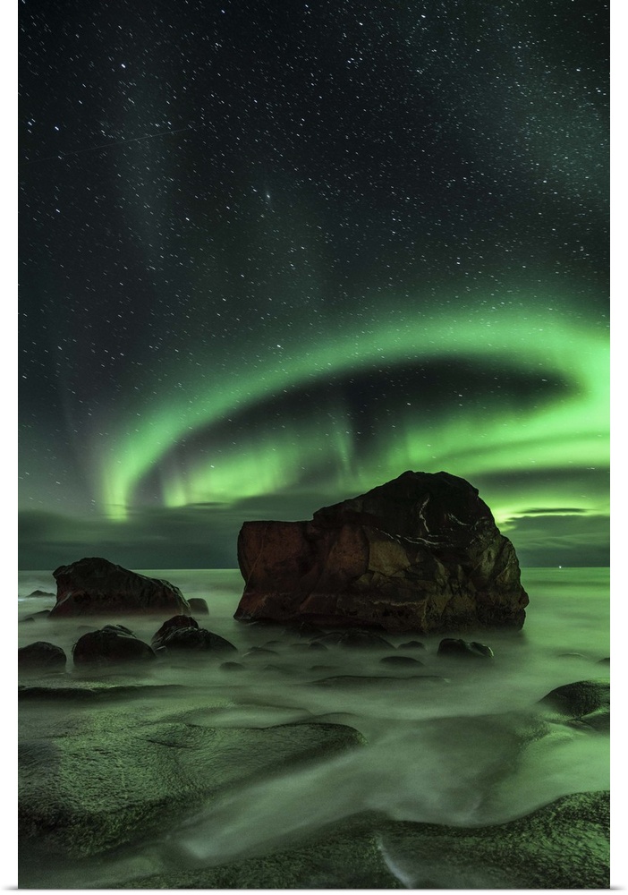 Ring-shaped aurora borealis over a boulder in the ocean, Norway.