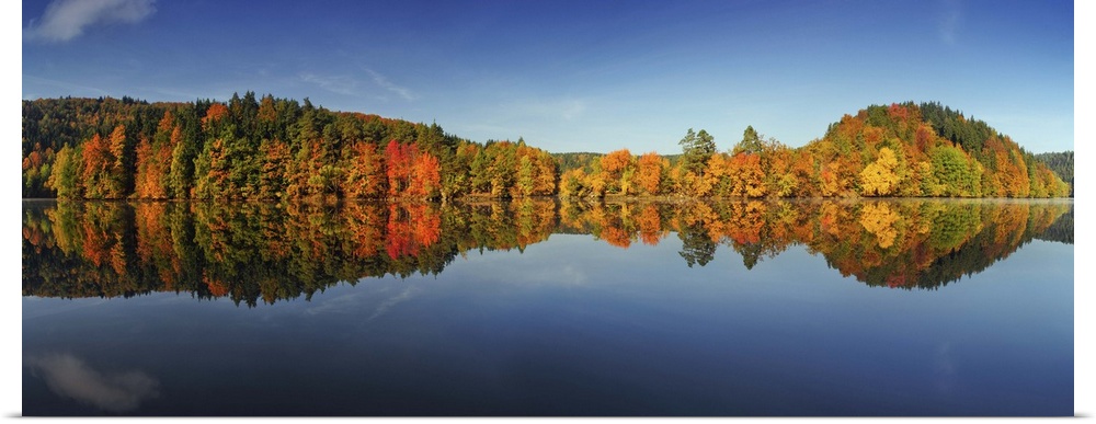 A forest in autumn foliage is reflected perfectly in the lake below.