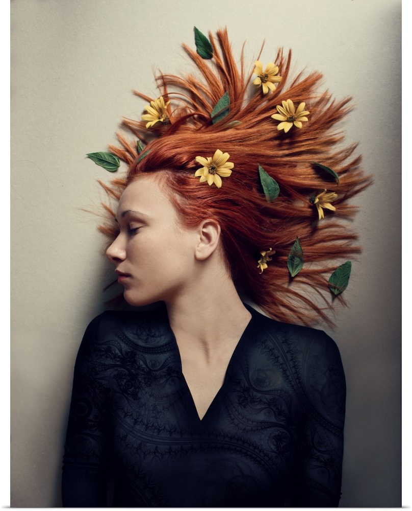 A portrait of a woman laying against a white surface with yellow flowers in her red hair.