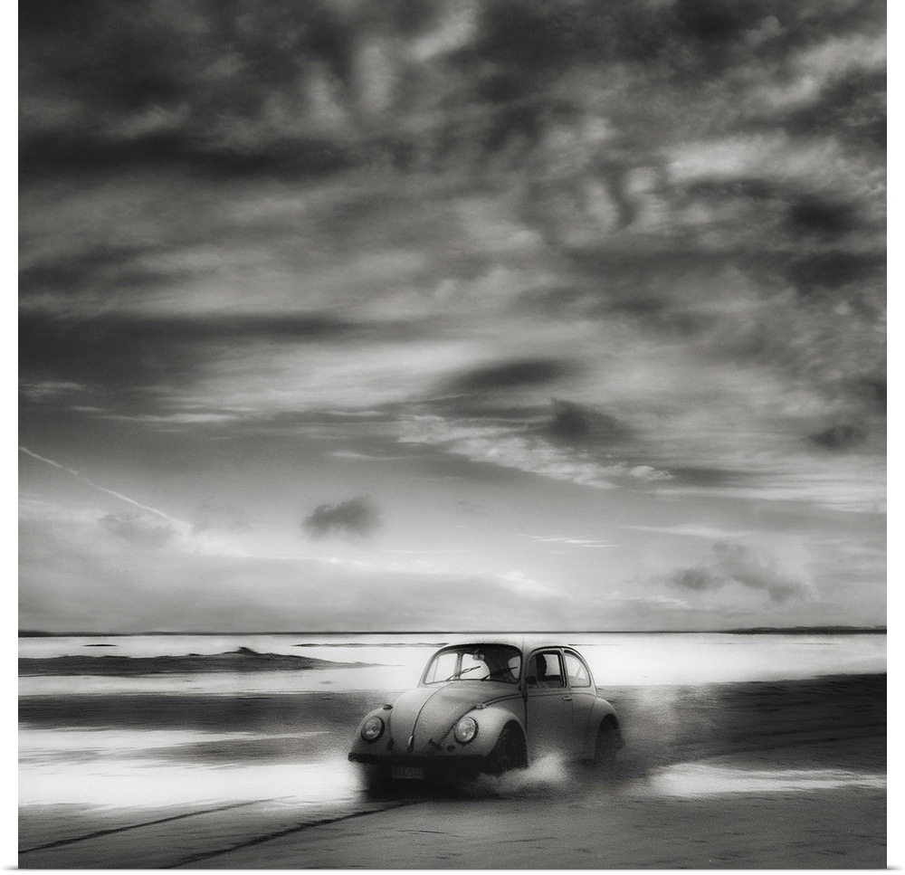 A Volkswagen Beetle driving down a sandy beach with stunning clouds overhead.