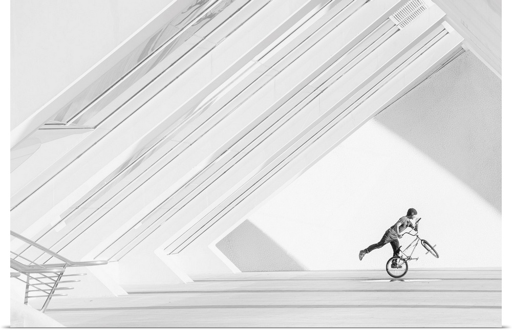 A black and white photograph of a guy riding a BMX bike under a geometric architectural structure.