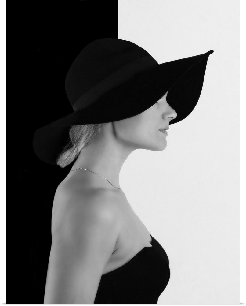 Portrait of a woman with a black hat, against a half black, half white wall.