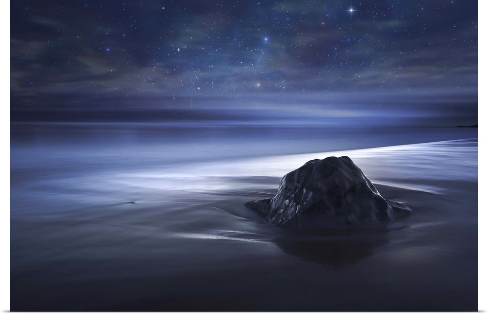 A rock on the beach in sand which appears smooth, under a starry night sky.