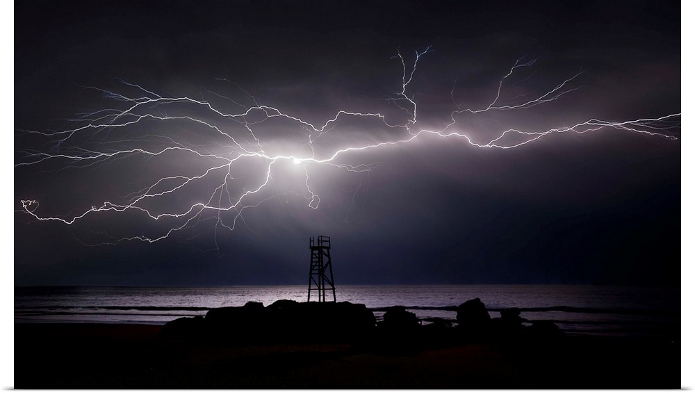 Giant, bright lightning bolt across the sky over a lifeguard tower on the beach by the ocean.