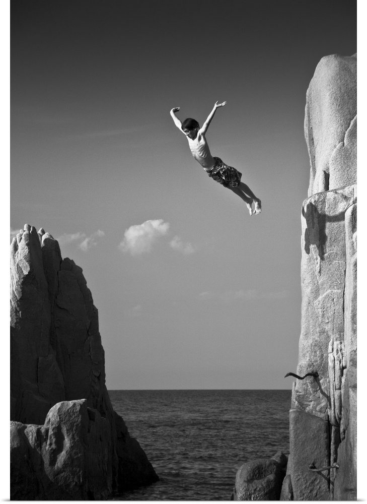 A young man leaping off a cliff into the ocean, Sardinia, Italy.