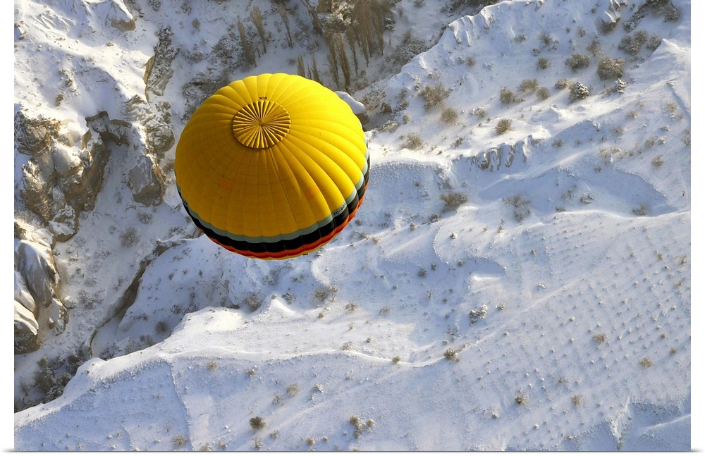 A yellow hot air balloon floats above the snow covered landscape of Cappadocia, Turkey.