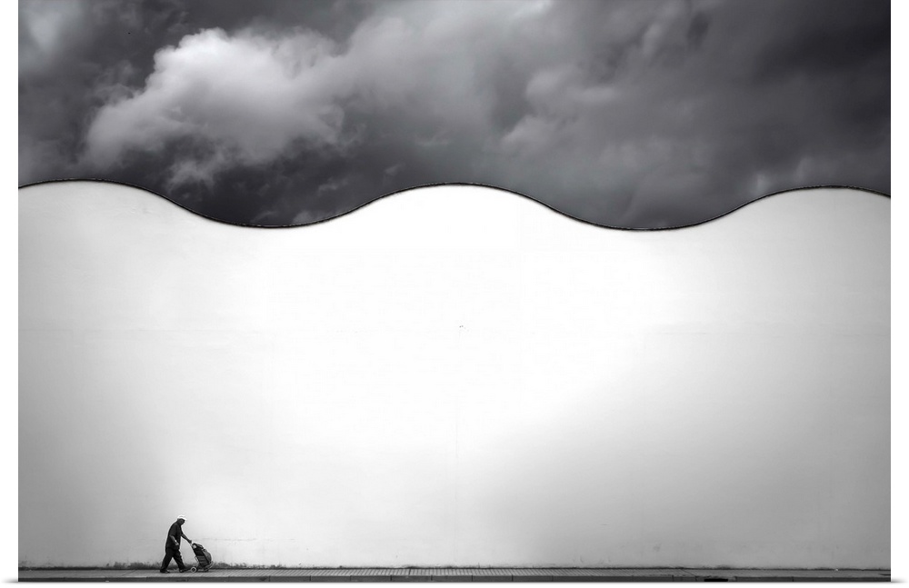 A man walks on a sidewalk below a wavy white wall, on a cloudy day.