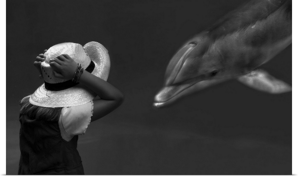 A girl holds her hat in excitement as a captive dolphin swims up to her in an aquarium.