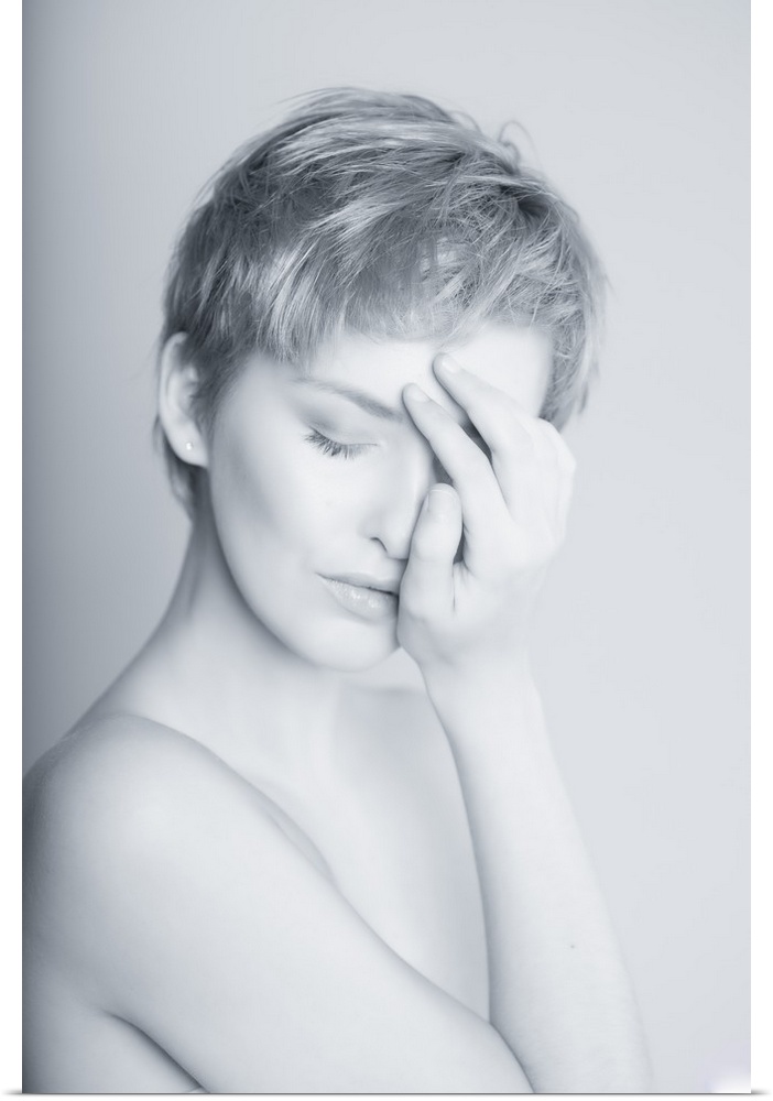 High key black and white portrait of a short haired woman covering half of her face with her hand.