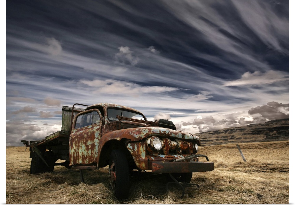 An old rusted truck sits unused in a field under a sky with dramatic clouds.