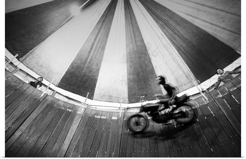 Motorcyclist riding on the wooden walls of a circus tent in a daredevil act.