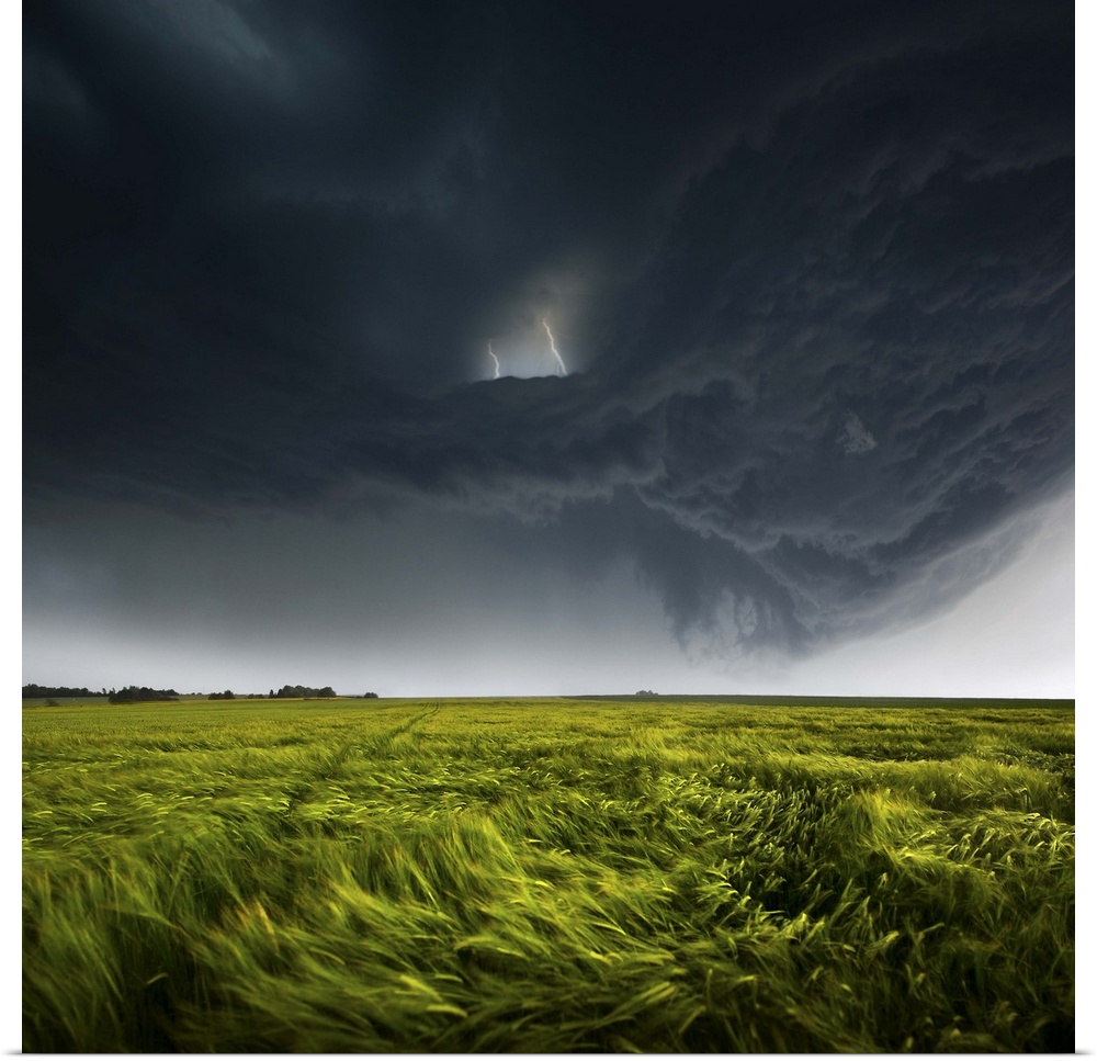 Menacing dark clouds producing lightning over a green field in the countryside of Germany.