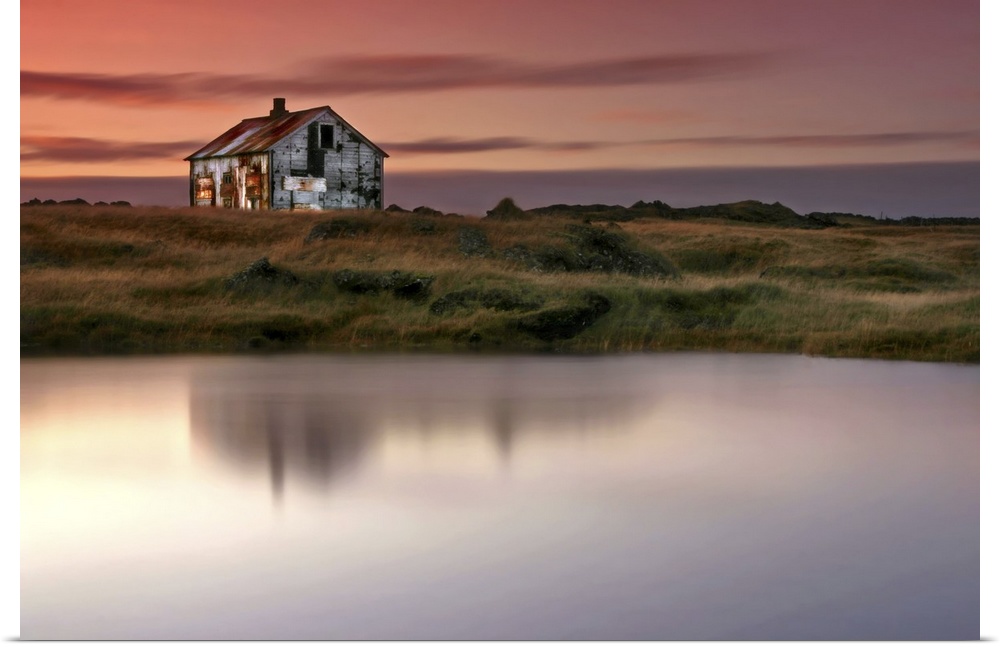 An abandoned farm house on the grassy shore by a lake in Iceland, at sunrise.