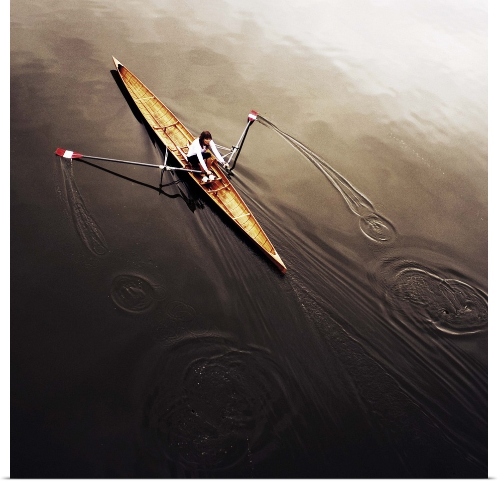 A female athlete rowing on still, dark water, leaving a small wake.
