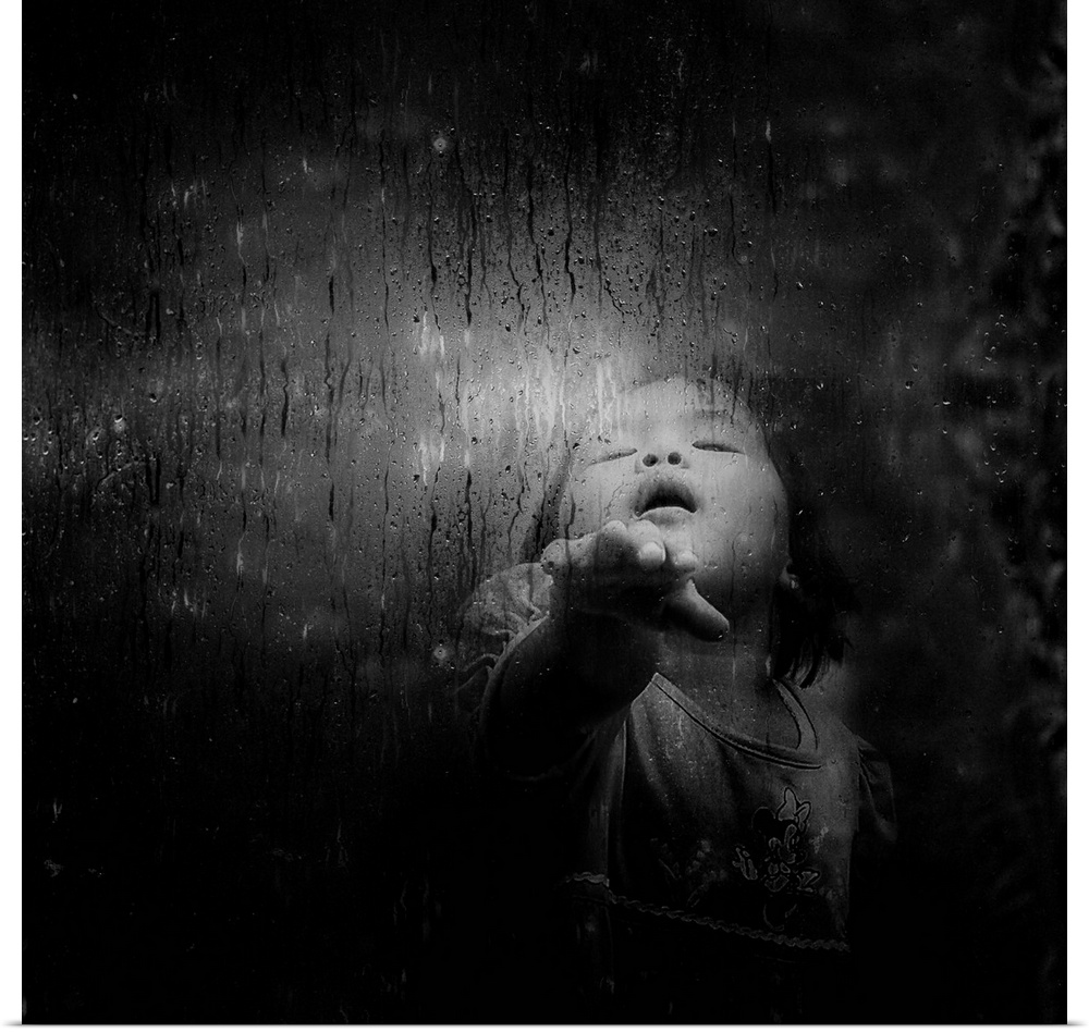 A young child puts her hand against a window with rain and condensation.