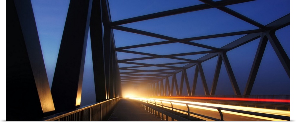 Light trails on a bridge with cross beams forming simple shapes in the morning.