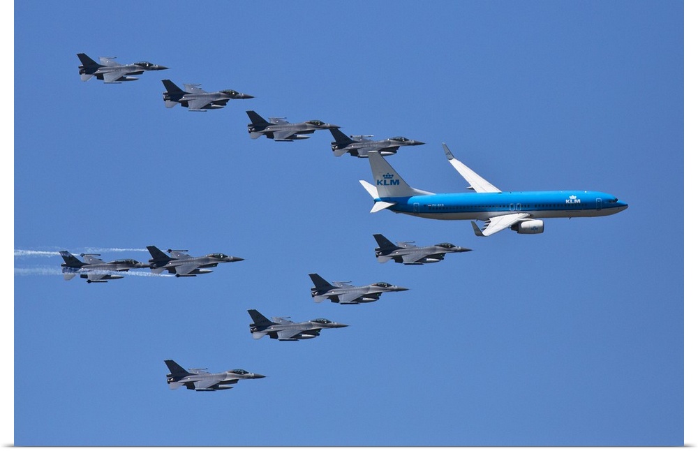 A fleet of grey jets fly in formation around a blue commercial airliner.